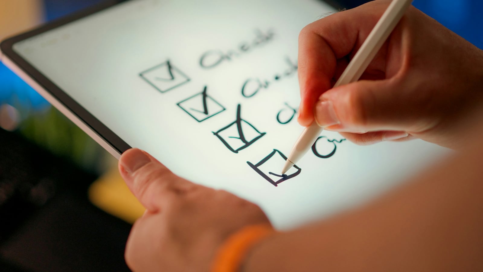 Close-up of a hand holding a tablet and ticking the last of four checkboxes with a white stylus, a handwritten checklist glowing on the bright screen against a blurred blue and amber background