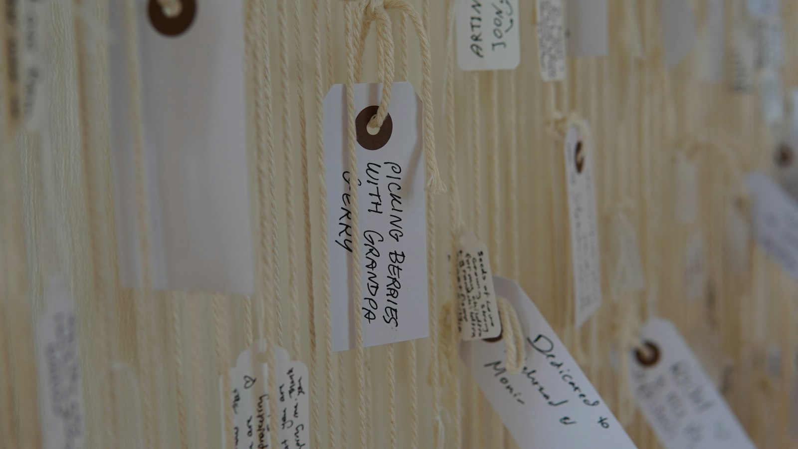 A wall of handwritten paper swing tags hanging on cream string, each one labelled with a different note