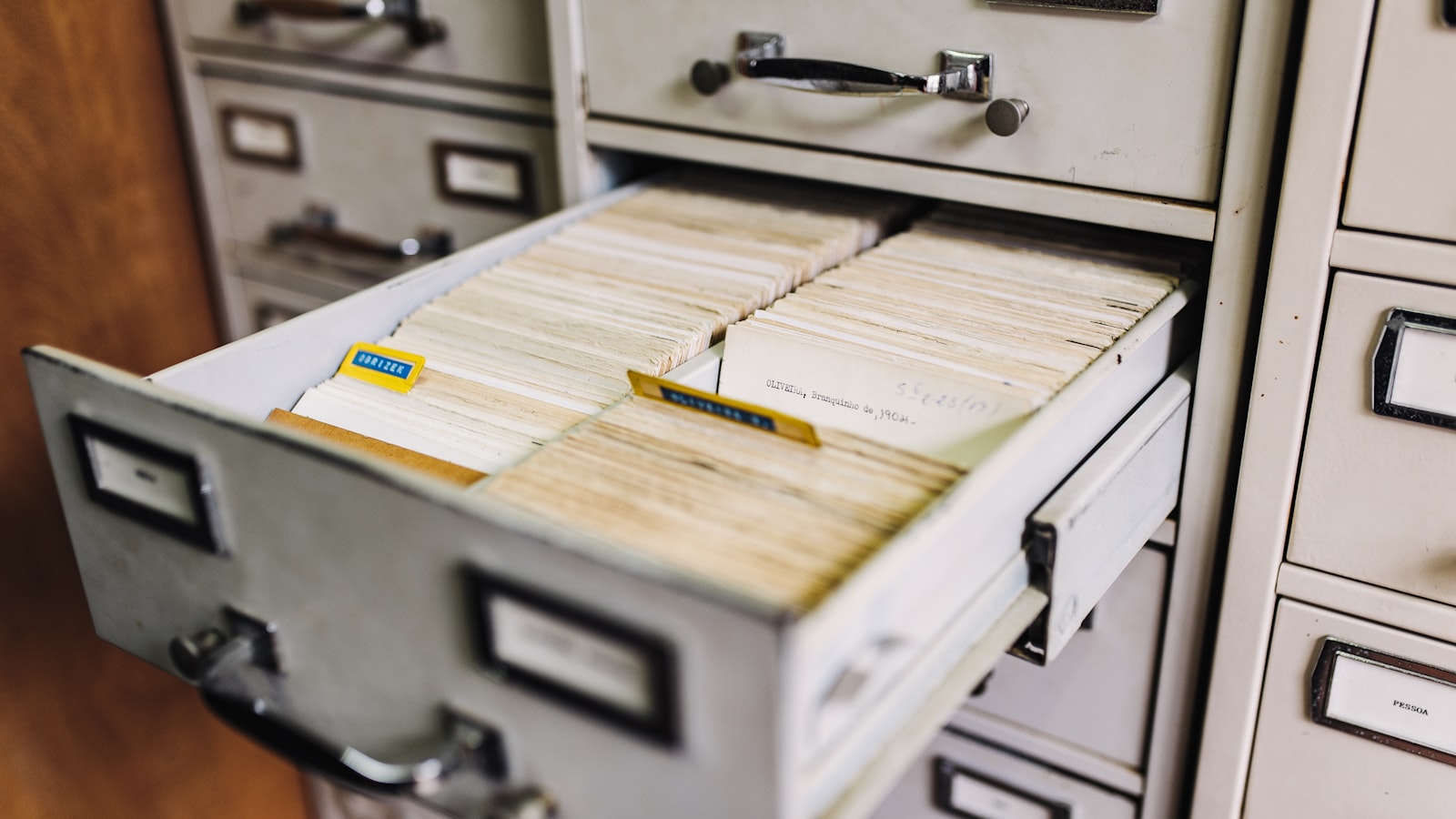 An open metal filing cabinet drawer packed with handwritten record cards, surrounded by other labelled drawers in an office records room