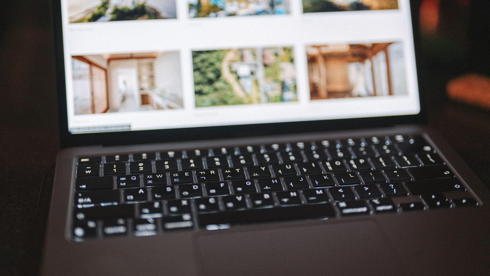 A laptop screen displaying a grid of real estate property listings - interior photos, an aerial view of homes, and architectural exteriors - on a property portal